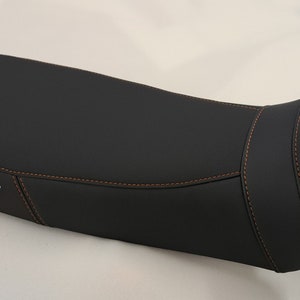 May include: Black motorcycle seat with orange stitching and the text "EMBROIDERY - HAFT" in white.