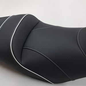 Op de afbeelding: Zwarte motorfietszadel met witte stiksels. Het zadel heeft een gecontourd ontwerp voor comfort.