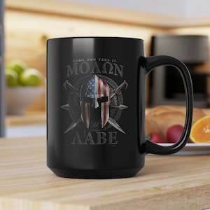 May include: Black ceramic coffee mug with a graphic of a Spartan helmet with crossed swords and an American flag. The text "Come and take it" is written above the helmet and "ΜΟΛΩΝ ΛΑΒΕ" is written below the helmet.