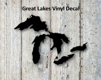 May include: Black vinyl decal of the Great Lakes on a white wood background. The decal is a silhouette of the Great Lakes, with the text "Great Lakes Vinyl Decal" above the image.