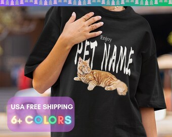 May include: Black t-shirt featuring a custom pet photo. The shirt displays a detailed image of a ginger cat with the text "Enjoy PET NAME" in a distressed white font. The top banner reads "CUSTOM PET PHOTO T-SHIRTS".