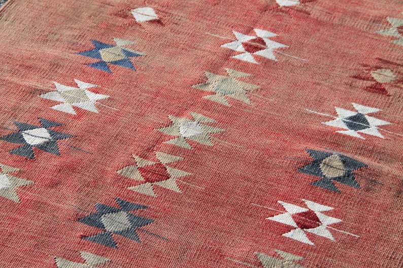 Op de afbeelding: Een rood tapijt met een geometrisch patroon in tinten wit, blauw en beige. Het patroon bestaat uit herhalende ruitvormen.