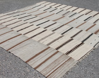 Op de afbeelding: Een groot, handgeweven tapijt met een patchwork-ontwerp. Het tapijt is gemaakt van natuurlijke vezels en heeft verschillende bruine en witte strepen.