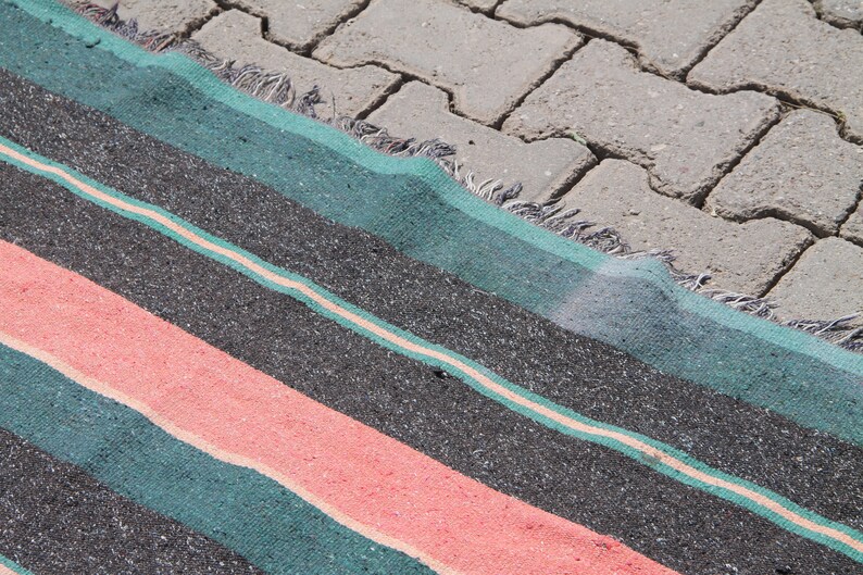 May include: A striped rug with teal, black, and pink stripes. The rug is lying on a gray concrete surface.