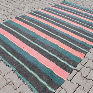 May include: A striped rug with pink, teal, and black stripes. The rug is made of woven fabric and has a fringed edge.