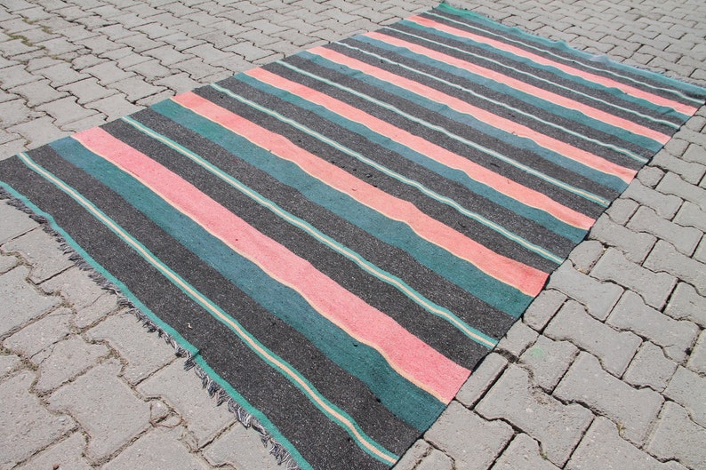 May include: A striped rug with pink, teal, and black stripes. The rug is made of woven fabric and has a fringed edge.