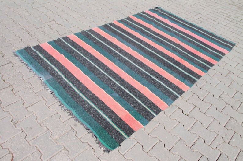 May include: A striped rug with pink, green, and black stripes. The rug has a fringed edge.