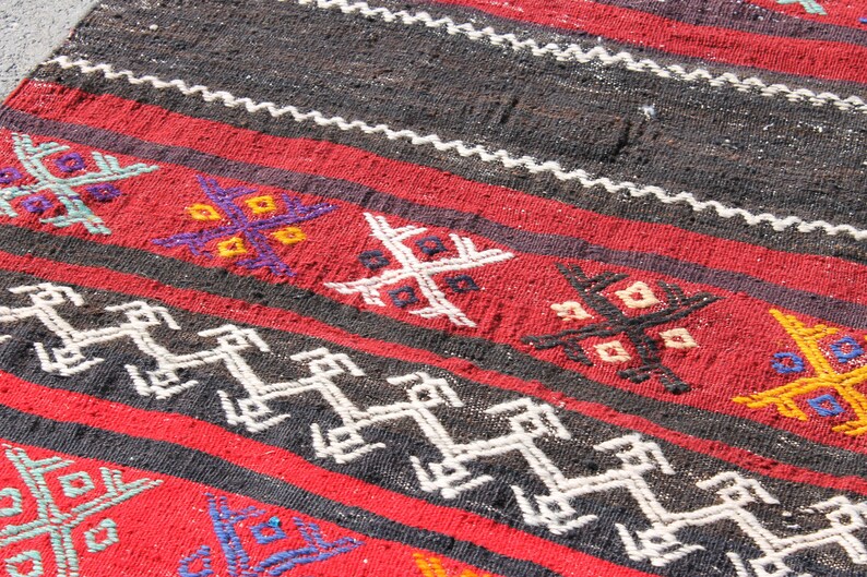 Pu&ograve; includere: Un tappeto rosso, nero e bianco tessuto con motivi geometrici. Il tappeto ha un design tradizionale con una variet&agrave; di colori e trame.