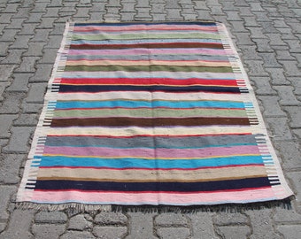 May include: A colorful striped rug with a variety of colors, including red, blue, green, and yellow. The rug is made of woven fabric and has a fringe on the ends.