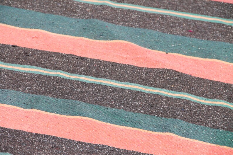 May include: Close-up of a striped fabric with alternating bands of dark gray, teal green, and light pink. The fabric has a textured, woven appearance.