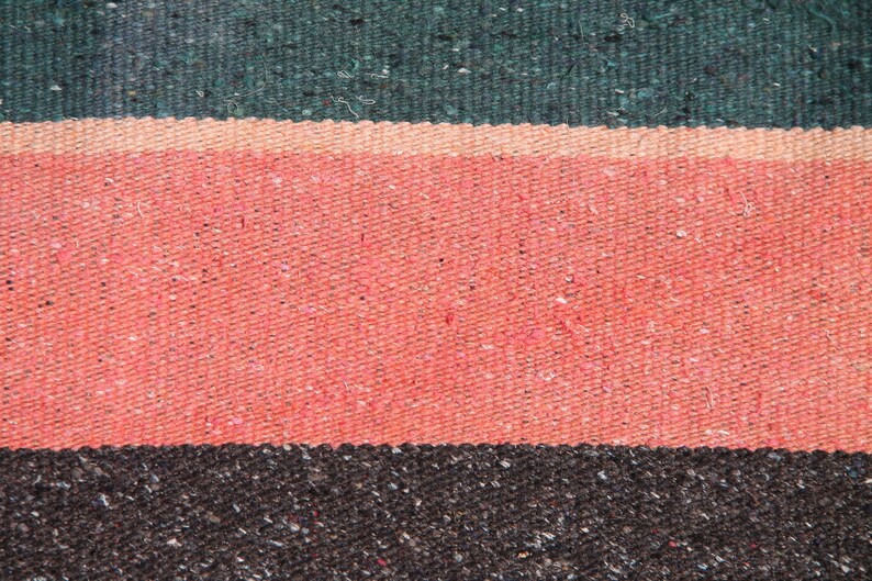May include: Close-up of a woven fabric with three horizontal stripes. The top stripe is dark green, the middle stripe is pink, and the bottom stripe is dark brown.