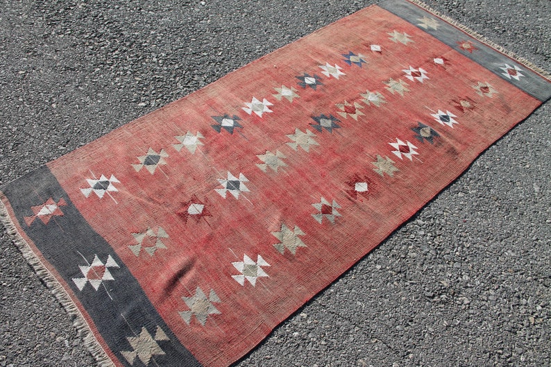 Op de afbeelding: Een rood, zwart en wit gestreept tapijt met een geometrisch ontwerp. Het tapijt heeft een franje rand en is gemaakt van wol.