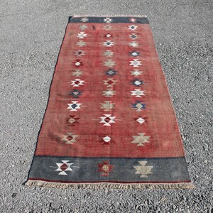 Op de afbeelding: Een lang, rood loper met een geometrisch patroon in tinten wit, blauw en bruin. De loper heeft een franje rand.