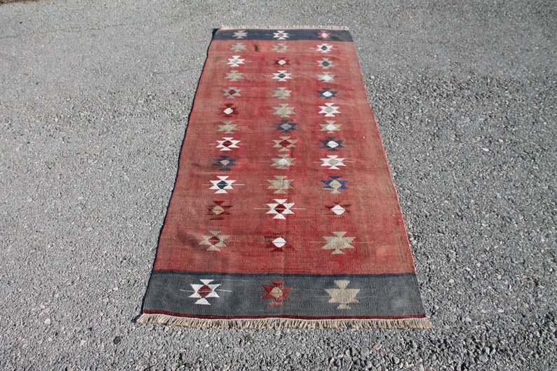 Op de afbeelding: Een lang, rood loper met een geometrisch patroon in tinten wit, blauw en bruin. De loper heeft een franje rand.