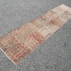 Pode incluir: Um tapete corredor vintage com um padrão geométrico em tons de vermelho, verde e bege. O tapete tem um aspeto desbotado e desgastado, o que lhe confere um caráter único.