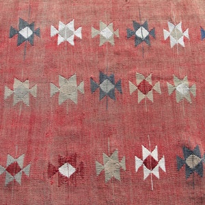 Op de afbeelding: Een rood tapijt met een geometrisch patroon van witte, grijze en blauwe ruiten en driehoeken.
