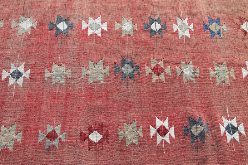 Op de afbeelding: Een rood tapijt met een geometrisch patroon van witte, grijze en blauwe ruiten en driehoeken.