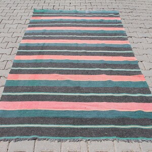 May include: A striped rug with black, pink, and teal stripes. The rug is made of a woven material and has a fringed edge.