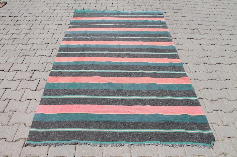 May include: A striped rug with black, pink, and teal stripes. The rug is made of a woven material and has a fringed edge.