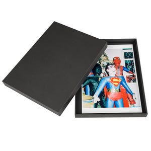 Könnte beinhalten: Eine schwarze Box mit offenem Deckel, die ein Foto einer Gruppe von Personen zeigt, die als Superhelden verkleidet sind. Das Foto zeigt eine Person, die als Superman verkleidet ist, eine Person, die als Spiderman verkleidet ist, und zwei weitere Personen, die als Superhelden verkleidet sind. Das Foto ist auf weißem Hintergrund gedruckt.