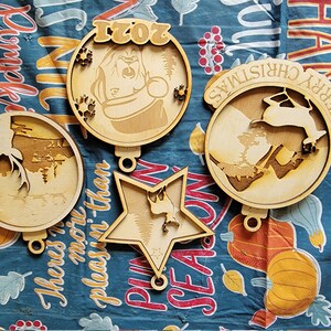 May include: Four wooden Christmas ornaments with various designs. One ornament features a bear with the year 2021, another has a reindeer with "Merry Christmas", and two others have nature scenes. Each ornament has a small hole for hanging.