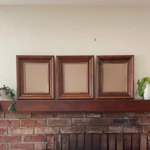 May include: Three rectangular picture frames made of dark brown wood with a visible grain pattern. Each frame features a stepped, tiered profile with a thin gold-toned inner border surrounding a plain, light brown rectangular center panel.