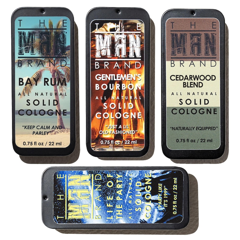 May include: An assortment of The Man Brand solid colognes in rectangular metal tins. The scents include Bay Rum, Gentlemen's Bourbon, Cedarwood Blend, and Life of the Party. Each tin is labeled with the scent name and the phrase "All Natural Solid Cologne."