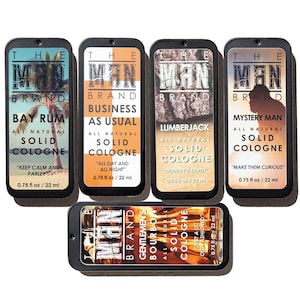 May include: A collection of five solid cologne tins from The Man Brand. Each tin features a different scent name, including "Bay Rum," "Business as Usual," and "Lumberjack." The cologne is 0.75 fl oz / 22 ml.