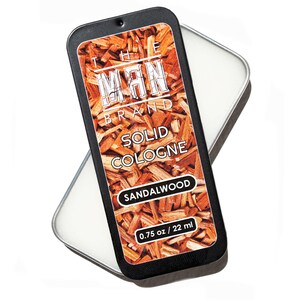 May include: A black rectangular tin of solid cologne from The Man Brand. The label features the brand name and the words "SOLID COLOGNE" and "SANDALWOOD" over a background of wood chips. The tin contains 0.75 oz / 22 ml of cologne.