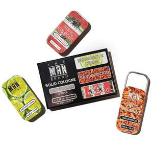 May include: An overhead shot of solid cologne tins and a variety pack box. The tins are rectangular with rounded edges, featuring labels with scent names like Sweet Tobacco, Sandalwood, and Bergamot & Cedar. The variety pack box includes three different scents.