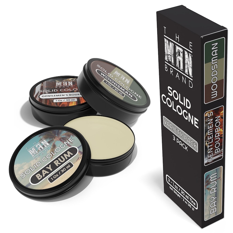 May include: Three 1-ounce tins of solid cologne in the scents Bay Rum, Woodsman, and Gentleman's Bourbon. The tins are black with white and gold labels. The packaging includes the text "The Man Brand" and "Solid Cologne Variety Pack 3 Pack".