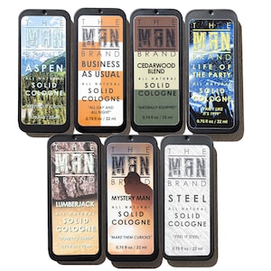 May include: An assortment of seven solid cologne tins from The Man Brand. Each tin features a unique label with a different scent name, such as "Aspen," "Business As Usual," and "Steel." The cologne is all-natural, with each tin containing 0.75 fl oz / 22 ml.
