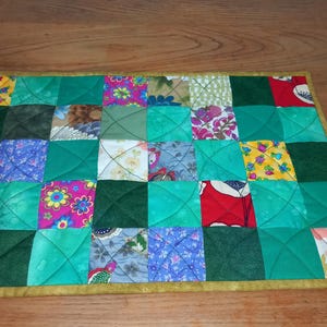 May include: A green, yellow and pink patchwork quilt with a yellow border. The quilt is made of squares of different fabrics, each with a different pattern.
