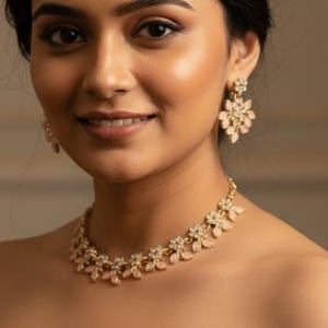 May include: A woman wearing a gold-toned necklace and matching earrings. The jewelry features a floral design with small, light-colored stones. The woman is wearing a gray off-the-shoulder dress.
