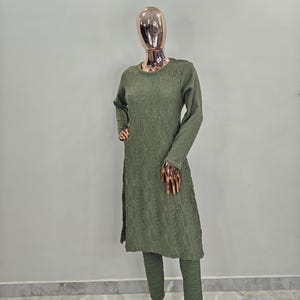 May include: A green sweater set with a long-sleeved top and matching trousers. The top has a textured knit and a round neckline. The trousers are slim-fitting and have a slightly flared leg.