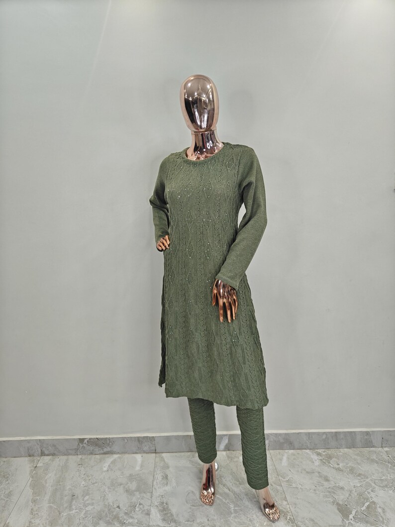 May include: A green sweater set with a long-sleeved top and matching trousers. The top has a textured knit and a round neckline. The trousers are slim-fitting and have a slightly flared leg.