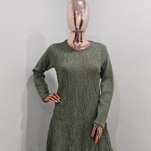 May include: A long-sleeved, green sweater dress with a diamond-shaped knit pattern. The dress has a round neckline and is adorned with small, sparkly embellishments.
