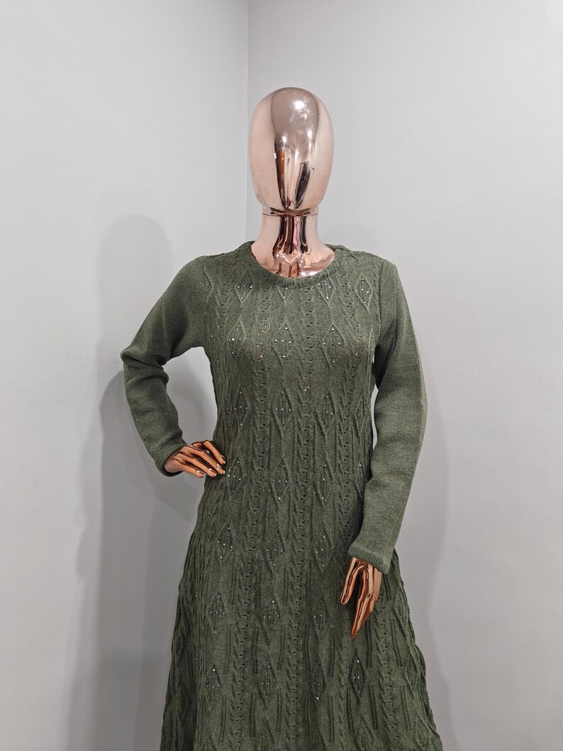 May include: A long-sleeved, green sweater dress with a diamond-shaped knit pattern. The dress has a round neckline and is adorned with small, sparkly embellishments.