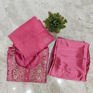 May include: A three-piece ensemble in a dusty rose hue. The set includes a tunic with intricate embroidery and sequin detailing, matching pants, and a coordinating scarf. A small potted plant with pink flowers sits nearby.