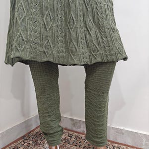 May include: A green knitted sweater dress with a cable knit pattern and matching leggings. The dress has a loose fit and a slightly flared skirt.