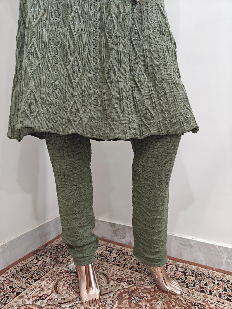 May include: A green knitted sweater dress with a cable knit pattern and matching leggings. The dress has a loose fit and a slightly flared skirt.