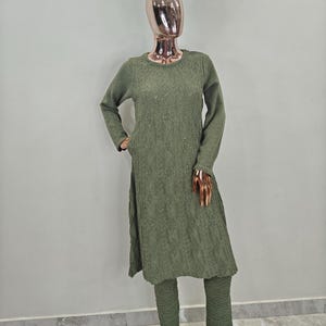 May include: A long-sleeved, olive green sweater dress with a diamond pattern and a matching pair of trousers. The sweater dress has a round neckline and a slightly flared skirt. The trousers are straight-legged and have a slightly cropped length.