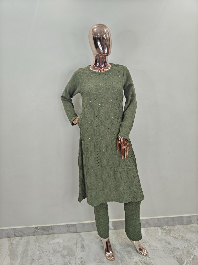 May include: A long-sleeved, olive green sweater dress with a diamond pattern and a matching pair of trousers. The sweater dress has a round neckline and a slightly flared skirt. The trousers are straight-legged and have a slightly cropped length.