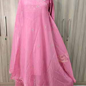 May include: A light pink, long-sleeved dress with intricate embroidery around the neckline and scattered across the fabric. The dress features a flowing, layered design, and is displayed on a mannequin. The fabric appears lightweight and semi-sheer.