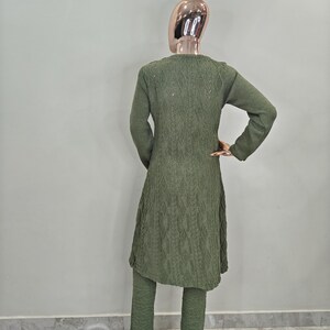 May include: A green knitted sweater set with a long cardigan and matching trousers. The cardigan features a cable knit pattern and the trousers have a textured design.