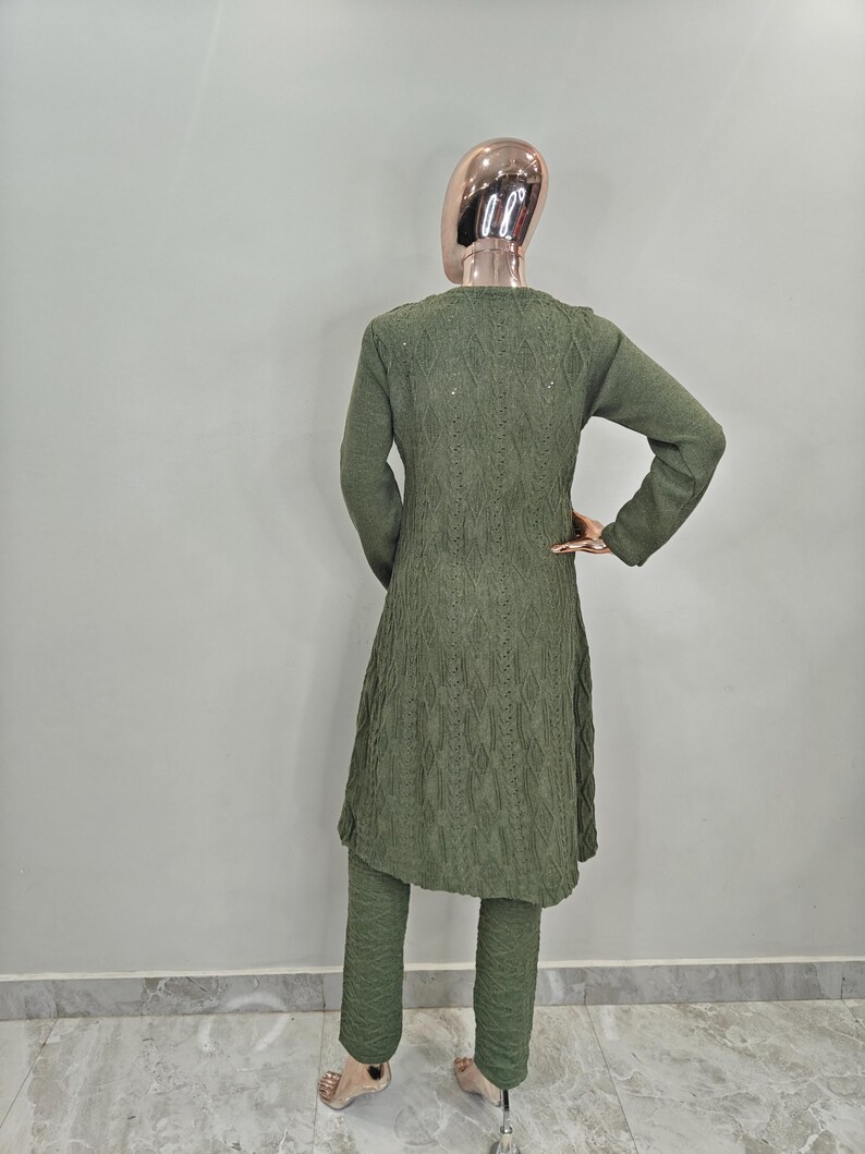 May include: A green knitted sweater set with a long cardigan and matching trousers. The cardigan features a cable knit pattern and the trousers have a textured design.