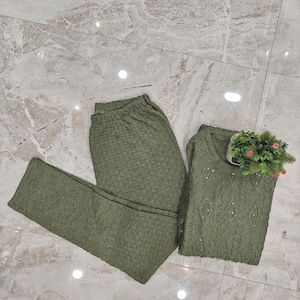 May include: A two-piece green knitted outfit with a long-sleeved top and leggings. The fabric has a textured, waffle-like pattern.