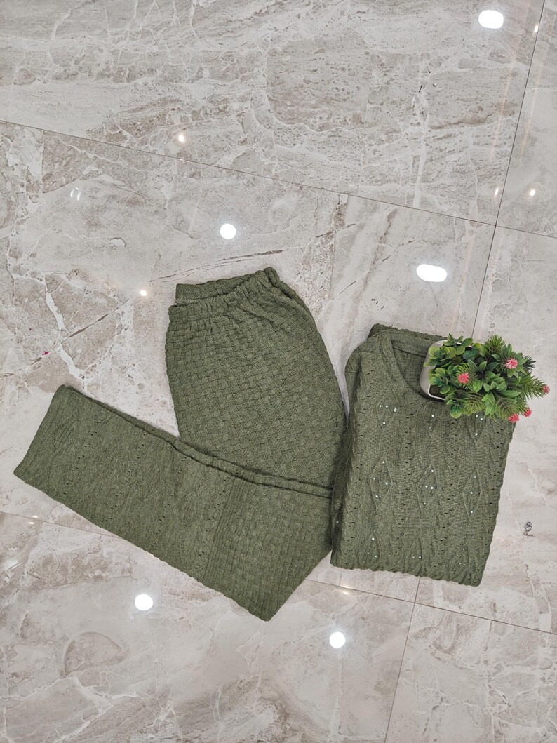 May include: A two-piece green knitted outfit with a long-sleeved top and leggings. The fabric has a textured, waffle-like pattern.