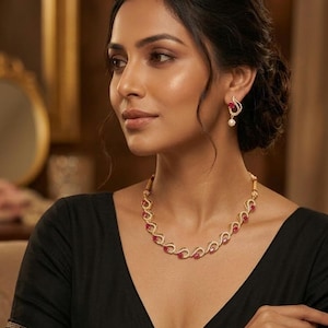 May include: A gold-coloured necklace and matching earrings set with red gemstones and small clear stones. The necklace has a curved design with the red stones set in the centre of each curve. The earrings have a similar design with a pearl drop.