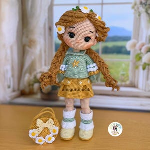 May include: A handmade crochet doll with long brown braids, adorned with daisy-like flowers. The doll wears a green sweater, yellow skirt, and white boots. A matching yellow basket with flower accents sits beside the doll. The doll is approximately 10 inches tall.